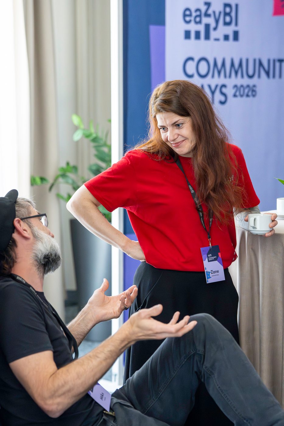 Two attendees chatting over coffee by the event banner
