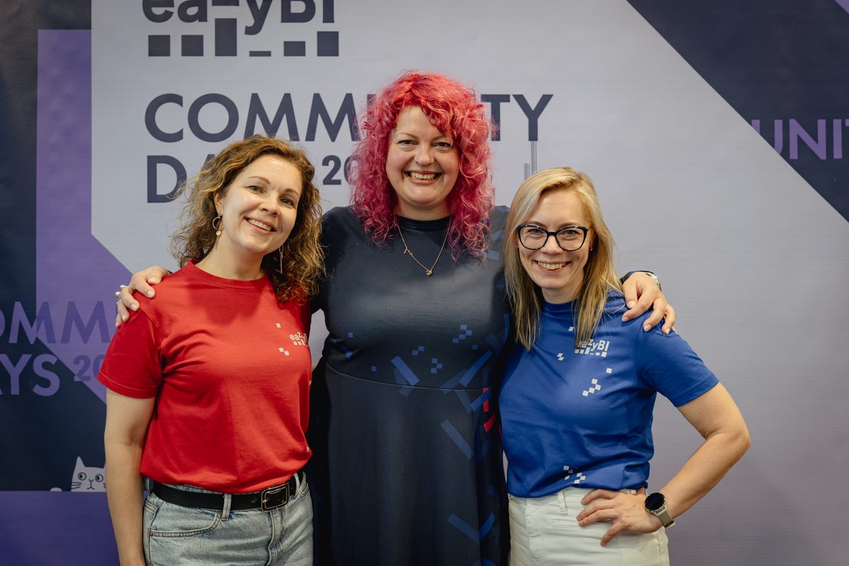 Three members of the eazyBI team smiling in front of the Community Days backdrop